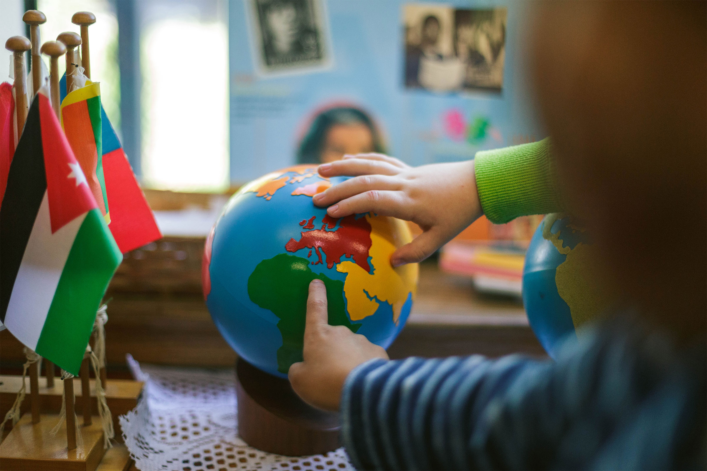 Children's hands pointing to globe of the world next to flags in Montessori classroom